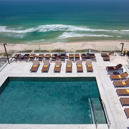 Windsor Marapendi Hotel ริโอเดจาเนโร ภายนอก รูปภาพ The photo shows a rooftop area with a swimming pool and several lounge chairs arranged around it. The pool has a clear blue surface, and the lounge chairs are positioned in a neat row, some with yellow cushions. In the background, you can see a beaut