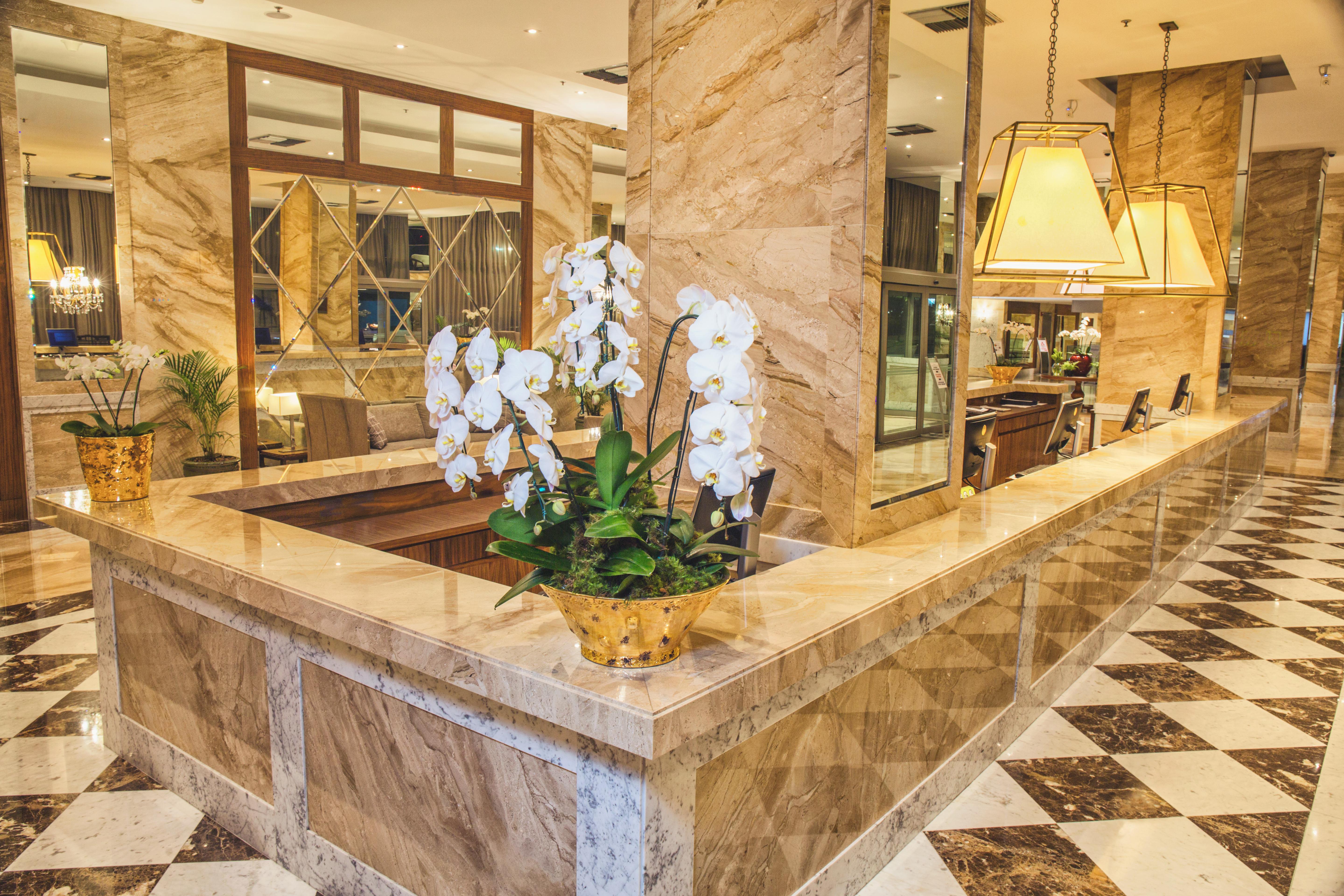 Windsor Marapendi Hotel ริโอเดจาเนโร ภายนอก รูปภาพ The photo depicts a luxurious hotel lobby featuring a polished marble reception desk. There are elegant white orchids arranged in a gold pot on the counter, adding a touch of sophistication. The surrounding interior showcases marble walls, stylish li